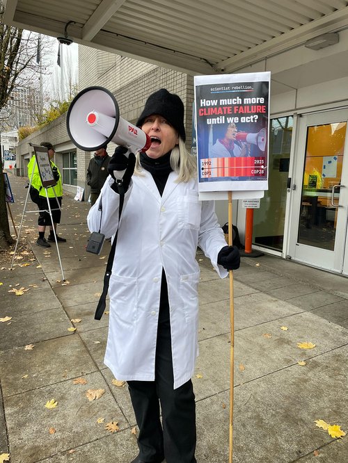a scientist talks into a megaphone while holding a sign that says how much more climate failure until we act