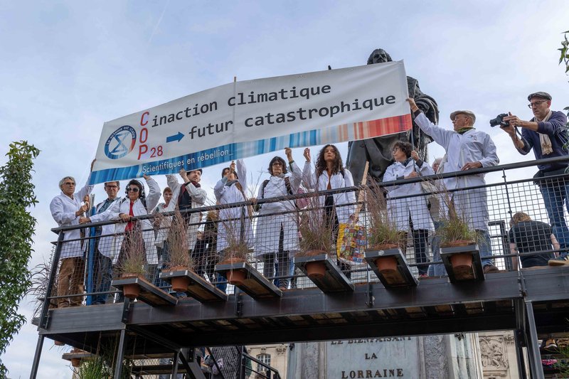 scientists in lab coats stand on a platform holding a banner that says inaction climatique futur catastrophique